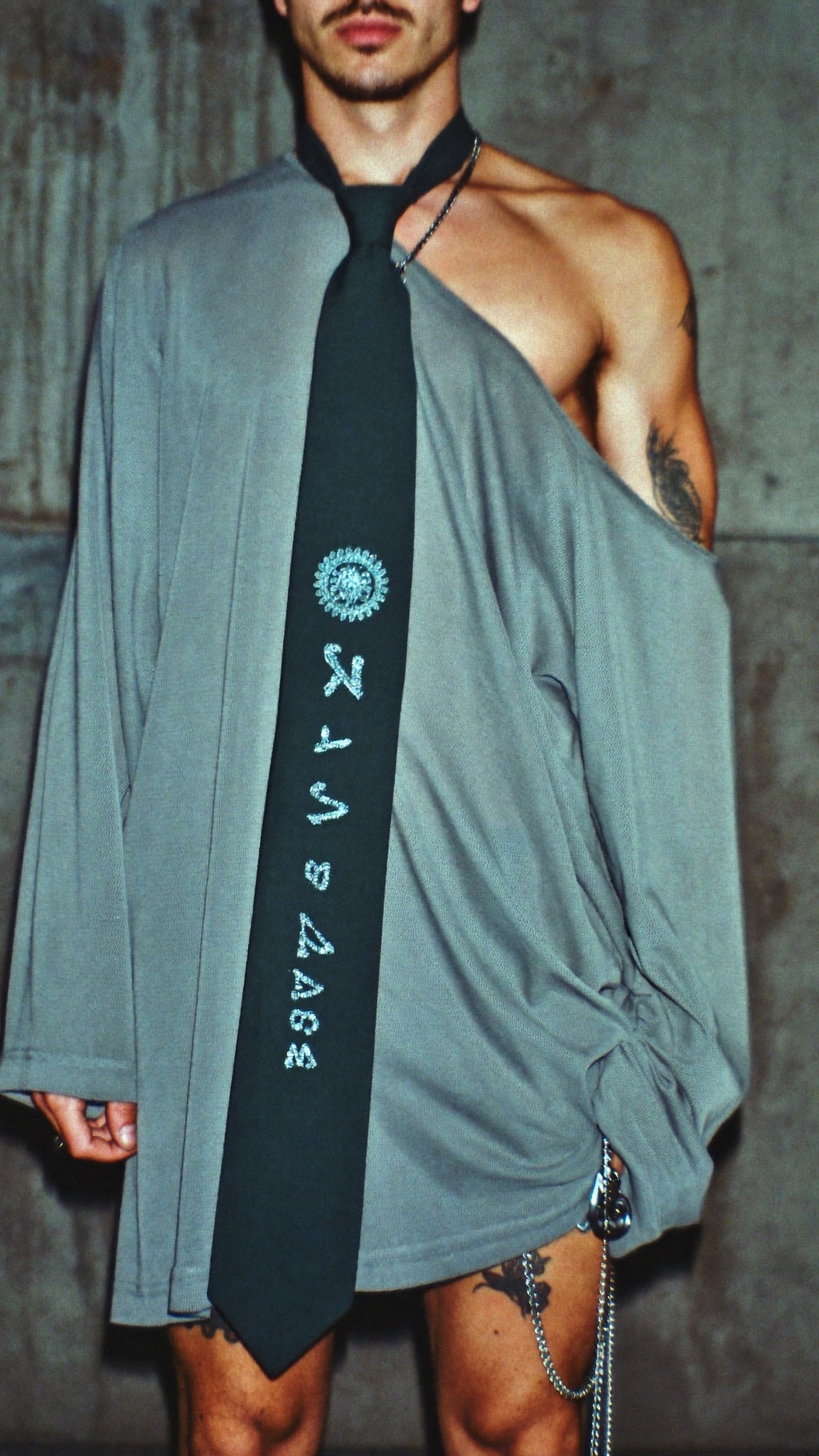 Male model in slouchy off-shoulder gray mesh with long tie and chains