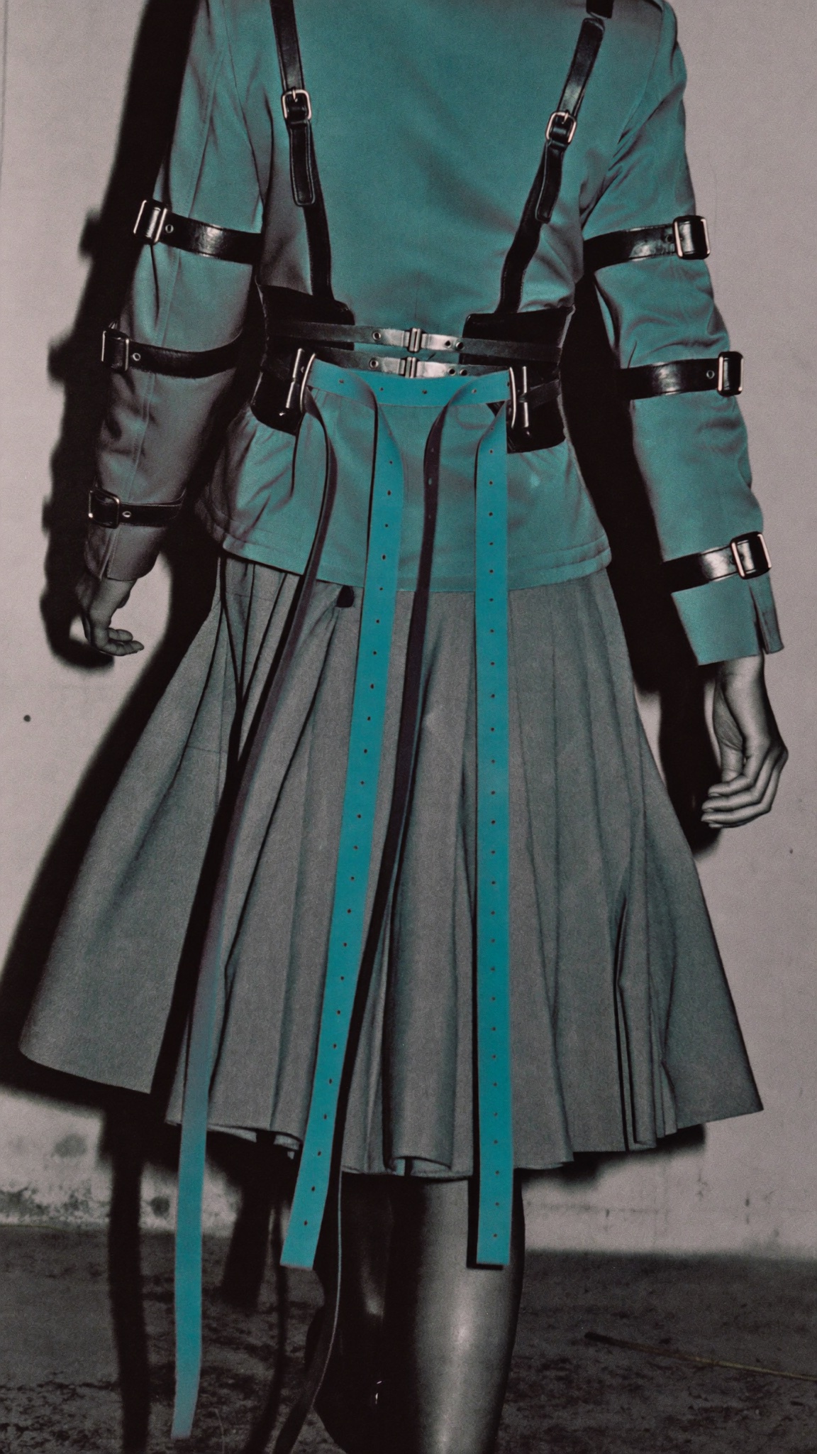 Back view of teal military jacket with crossed buckle straps and hanging belt tails