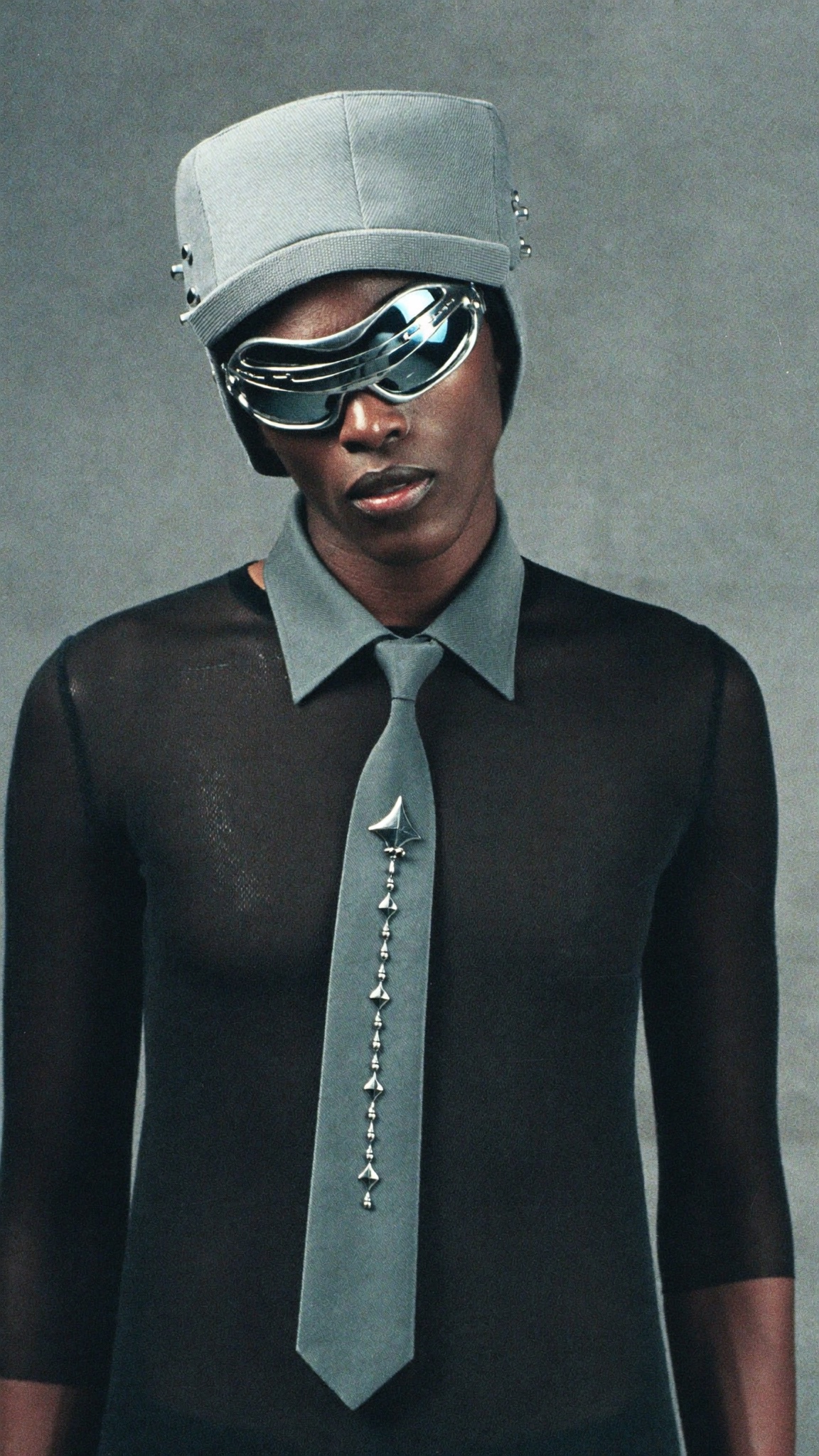 Portrait with gunmetal sunglasses, structured hat, mesh top and skinny tie